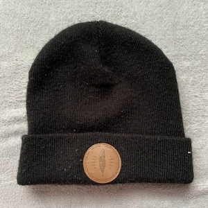 Svart Beanie - svart beanie med brun detalj, ganska använd men bra skick tror jag köpte den på intersport