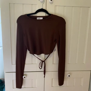 Brun topp - Jättefin chokladbrun croppad topp, i blankt tyg, perfekt nu till hösten!🍁 Ryggen är öppen och knyts längst ner, se andra bilden.  Väldigt lite använd så fint skick!  Hör av dig vid intresse eller fler bilder. Köpare står för frakt.