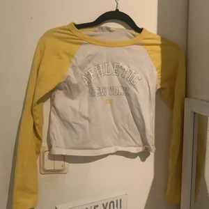 Jag säljer en långarmad topp - Den är gul om armarna och på framsida står det ATHLETIC NEW YORK.Den är använd. 