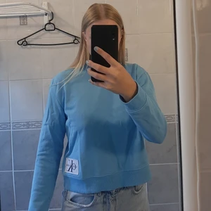 Blå Calvin Klein tröja - Klarblå Calvin Klein jeans tröja i storlek XS. Endast använd ett fåtal gånger så den är så gott som ny. Modellen är lite croppad 💙