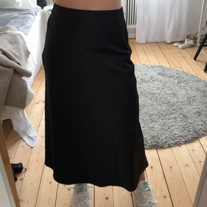 Svart långkjol i satin - Svart långkjol i satin från Lindex! Den har tyvärr fått ett litet märke vid en söm vid höften vilket syns på bild 2, annars är den i fint skick! Frakt tillkommer på 66kr.