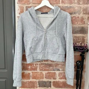 Zip Hoodie  - Säljer denna mjuk zip hoodie från Brandy Melville i ljus grå. Den är lite cropped. Bra skick 