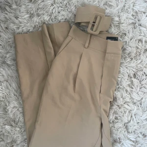 Kostymbyxor Gina 38 - Ett par höga kostymbyxor från Gina Tricot i strl 38. Kan användas med eller utan bältet som syns på bilden! Väldigt snygga att ha som oversize då de är ganska smala i midjan. 