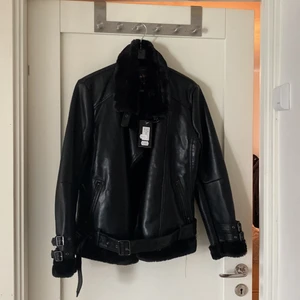 Bikerjacka med pälsdetaljer - Helt oanvänd fuskläder jacka med pälsdetaljer runt kragen och ärmarna. Spännen vid ärmarna. Pälsfodrad inuti så den är nog ganska varm. Köpt för 995 kr. 