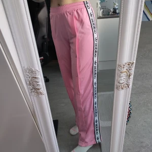 Rosa Adidasbyxor från Kylie Jenners kollektion - Rosa adidasbyxor från deras samarbete med Kylie Jenner. Det är popperpants och går att knäppa hela vägen upp. Två fläckar nere vid ändarna men märks inte när man har byxorna på sig. Storlek S men passar även mig som oftast har M. 