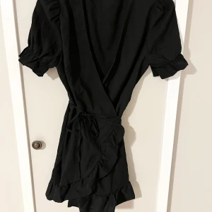 Svart omlottklänning  - Fin svart omlottklänning i ”linnematerial”. (Är i strl L egentligen men är mer utformad som en M)