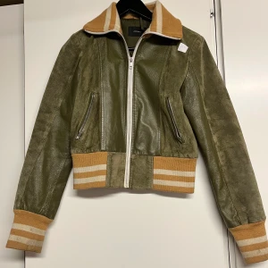 Grön 70-tals skinnjacka - Coolaste jackan från Vero Moda i sportig 70-talsstil! Köpt av sickansplagg här på plick men kommer inte till användning tyvärr :( Assnygg grön färg med vita o gula muddar, så trendig!! 