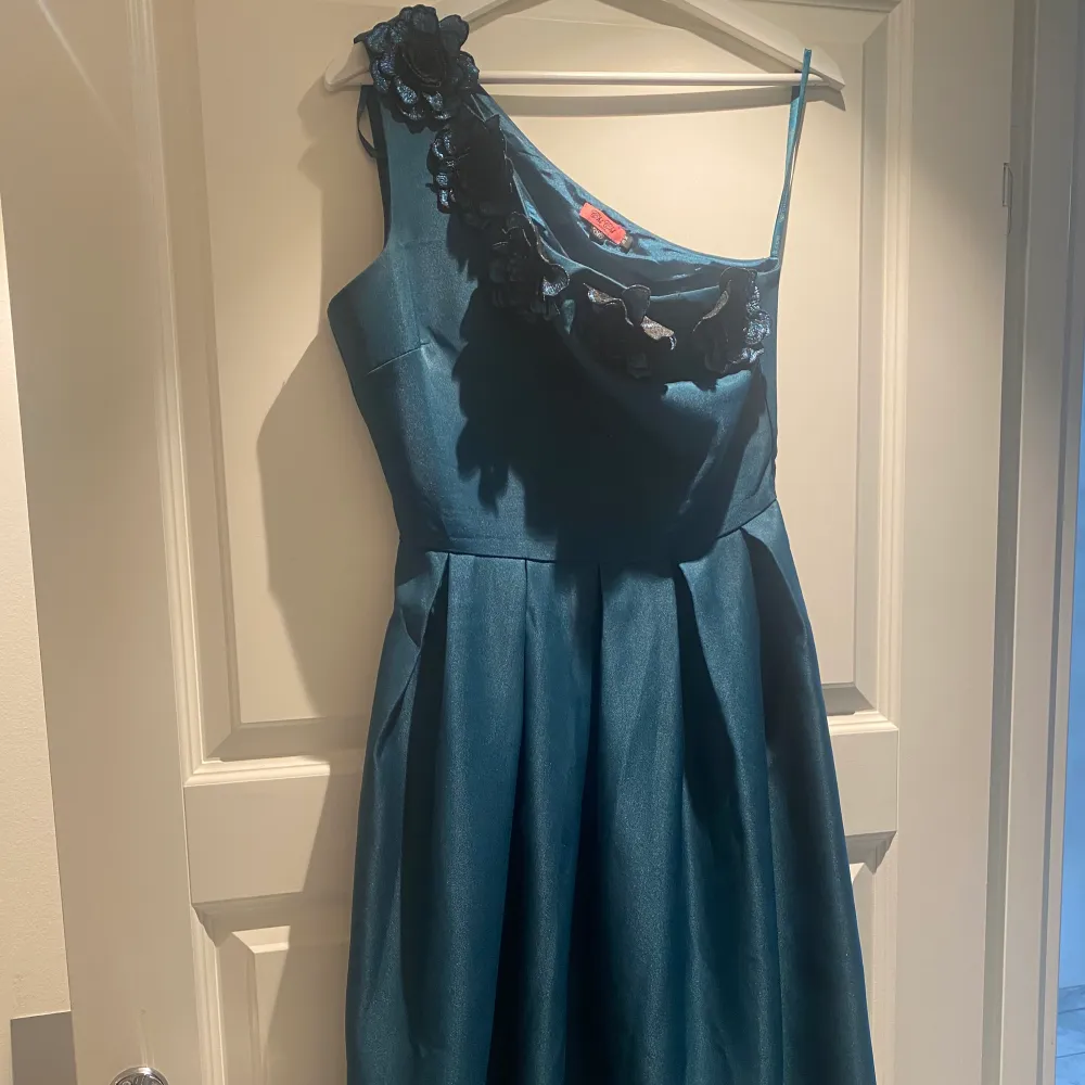 En blå klänning med blommor upptill som endast är använd 1 gång. Klänningen är i storlek 36 och knälång med en mycket bra passform och ett axelband i modellen. Den passar perfekt för fester/evenemang eller liknande. Priset kan diskuteras. . Klänningar.