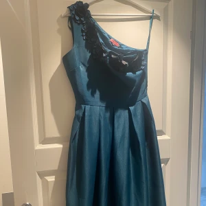 Blå klänning  - En blå klänning med blommor upptill som endast är använd 1 gång. Klänningen är i storlek 36 och knälång med en mycket bra passform och ett axelband i modellen. Den passar perfekt för fester/evenemang eller liknande. Priset kan diskuteras. 