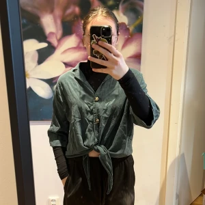 Croppad skjorta - En mörkgrön croppad skjorta från Lindex i strl S. Den har tre knappar och knytning längst ner. 