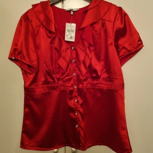 Röd satin blus  - Superhärlig röd blus i satin. Helt ny och oanvänd, prislapp och extra knappar kvar. Perfekt fest-blus! (Bild 2 tagen med blixt). Kolla gärna in mina andra annonser❤️