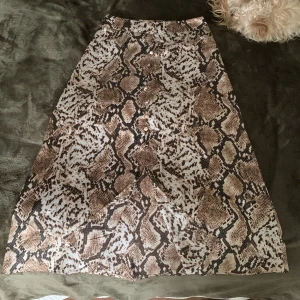 Satinkjol - Säljer den här fina satinkjolen med brunt ormmönster på då det är ej min stil längre. Den är använd några gånger. Kjolen har en liten slit på framsidan längst ner och en liten dragkedja på sidan. Saknar en knapp precis ovanför sliten men det märks inte🤎🤍