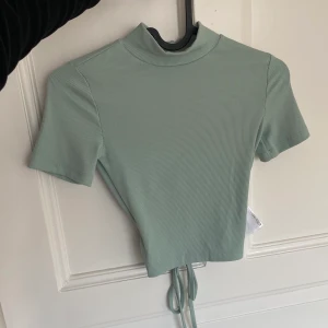 Topp - Tröja från Ginatricot, den är ljusgrön och har öppen rygg så man kan knyta hur hårt man vill ha det. Använd nån enstaka gång då den blivit för liten. Storleken är XS🤎