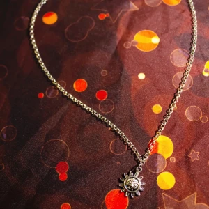 Halsband med solhänge - Handgjort (av mig) halsband med ett metallhänge i form av en söt liten sol. Halsbandet består av en kedja med låsmekanism högst upp. 🌞