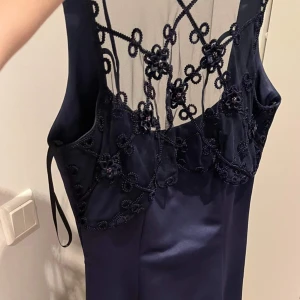 Balklänning med spetstyg fram  - Mycket vacker blå balklänning med spets fram och dragkedja samt halvöppen rygg med tre knutar. 