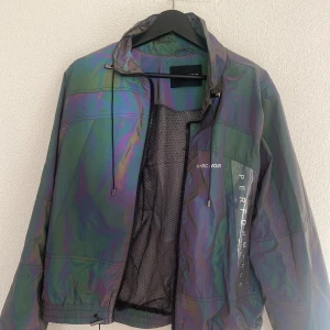 M+RC Ghost Dark Reflective Rainbow Track Jacket - Synliga flaws kan ses runt kragen pga dragbandet.