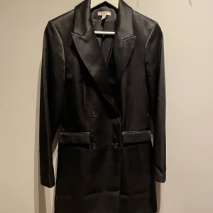 Oanvänd Klänningkavaj i strl XS/S - Superfin kavaj som går att använda som en klänning. I svart, glansigt material. Inga slitage, som ny. I strl S men passar bra till en XS. Från H&M