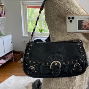 Svart väska - Lägger upp igen pga förra köparen drog sig ur. Obs bud är bindande!! Säljer denna väska med snygga detaljer såsom spännen och nitar. Dragkedjan till ett innerfack är trasig+ några enstaka fläckar på innerfodret, i övrigt toppskick💕💕💕