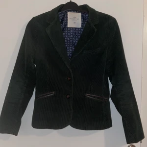 Kavaj blazer Manchester medium - Mörkgrön kavaj i superfint skick med detaljer i skinnimitation. Står storlek 42 men är mer lik en 38/medium. Färgen är helt jämn och fin i verkligheten, svår att fånga på bild. 