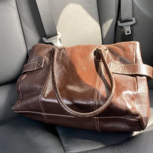 Mörk brun vintage väska - Säljer denna jätte söta mörk bruna vintage väskan av äkta läder som är köpt på second hand. Den är lite sliten men fortfarande jätte söt och lätt att styla. inut i finns det små fack samt ett stort fack med blixtlås. Kan mötas upp i Ystad - Malmö/Lund annars får man stå för frakt själv 🥰 