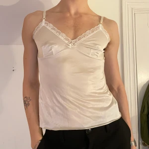 Vit vintage cami spets linne satin - Vit vintage cami i satinliknande material med spets längs halsringningen, en rosett och justerbara band 🤍🤍 en mer unik twist på en basic!!