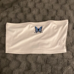 Topp utan ärmar - En fin vit tröja utan ärmar med en blå fjäril 