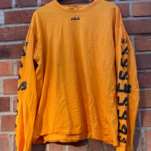 Orange Fila tröja perfekt till skater stilen - En fila tröja med lite slitage som är perfekt till en oversized skaterstil. Tröjan har snygga tryck där det står ”Fila Collab” i svart stil i kombination med ett fila märke vid halsen