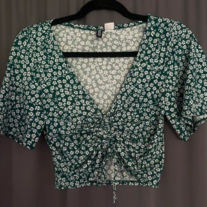 Grön sommar t-shirt - Jättesnygg grön t-shirt med vita blommar och går att spänna i mitten som man ser på andra bilden! Säljer då den inte passar längre💖 Köparen står för frakten!