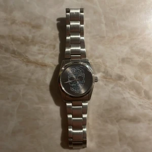 Zadig & Voltaire klocka  - Klockan är använd i ca 6 månader. Tecken på små repor finns på baksidan(syns i bild). Klockans bredd är 33mm. Min handled är 18 cm i omkrets men medföljer även bitar att göra klockan längre eller kortare. Köpte klockan för 2200 kr.