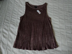 Oanvänd glittrig topp/linne med fint fall, plommon/guld, storlek S - Skitsnygg glittrig topp som är oanvänd. Den är brun/plommonfärgad med guldfärgat glitter/skimmer. Mjuk och ganska tunn med fint fall. Perfekt överdel till fest/jul/nyår. Storlek S.