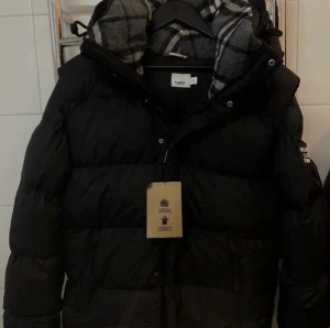 Burberry puffer jacka - Autentisk burberry jacka som även kan bli till väst om man drar av ärmarna. Nyskick utan skador elr märken. Jackan har och nfc. Du får med äkthetscertifikat, dustbag och taggar. Säljer den pågrund av att den är i för stor storlek..