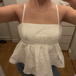 Vitt linne med öppen rygg och knytning  - Säljer mitt ikoniska Ginalinne! Använt flera gånger men i bra skick. Justerbara band samt knytning i ryggen, blommor struktur!