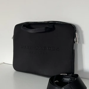 Marc Jacobs datafodral + axelband - Datafodral med värdering och vattentätas dragkedja. Finns även extra fack på baksidan med dragkedja samt axelband. Väldigt bra skick! 