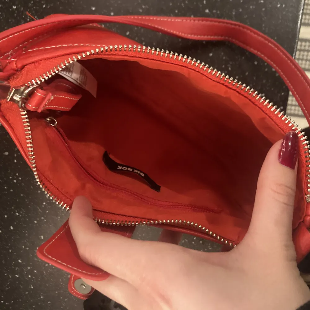 En baguetteväska i en jättefin röd färg. Endast använd en gång så i väldigt bra skick. Har ett fack med dragskejda i väskan.. Väskor.