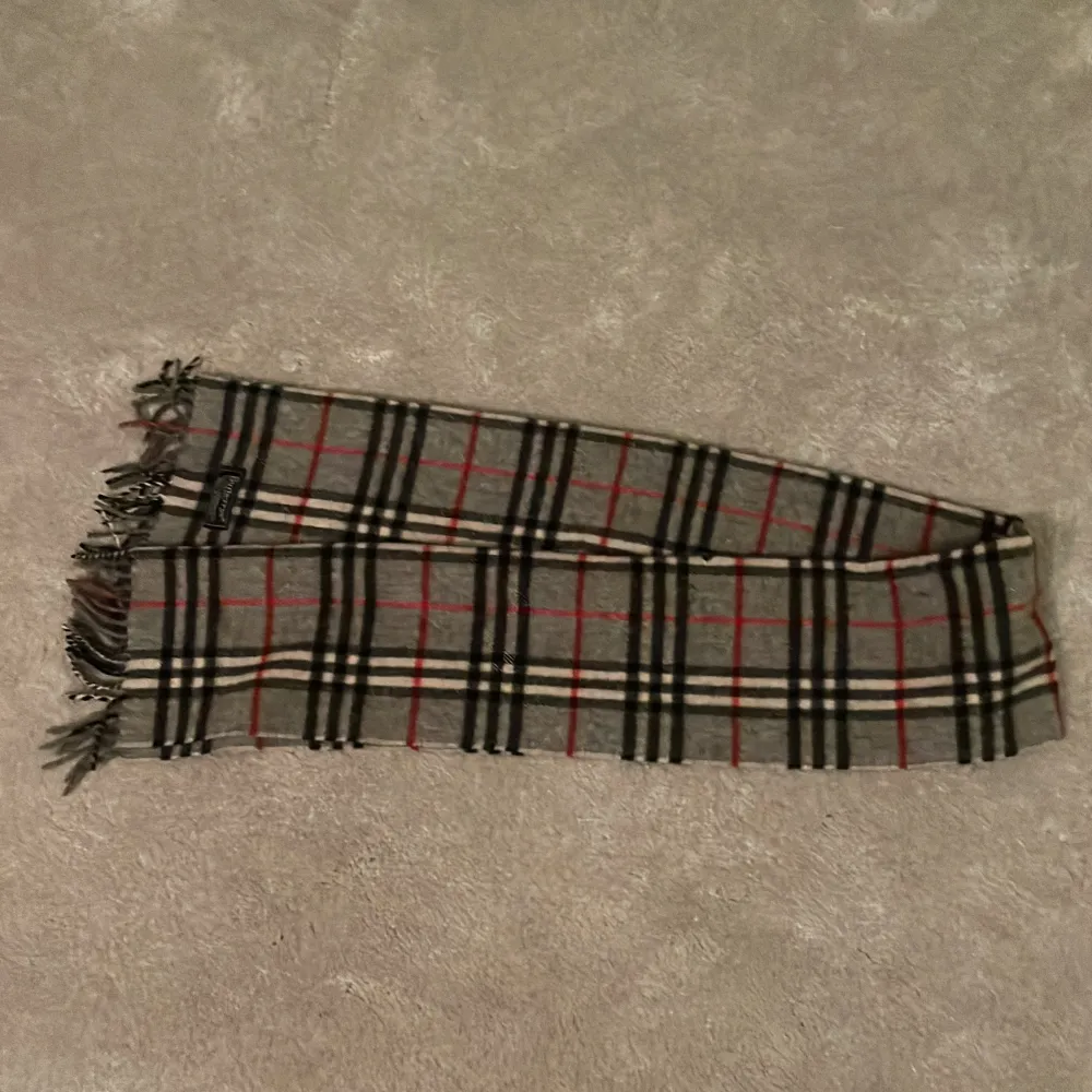 Säljer min burberry halsduk som jag fick i julklapp för 2 år sen! Den är grå med röda, vita och svarta ränder på kan också byta mot saker! Skick 7/10 det finns några små hål men syns inte vid användning  Skriv om frågor eller liknade!. Accessoarer.