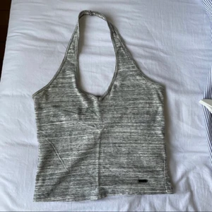 Halterneck topp - Gulligt gråmelerat linne från Hollister i storlek XS. Har använts några gånger men är i mycket bra skick.  Axelbandet träs runt huvudet så den sitter som en rem och sedan är den rätt djup i ryggen och rätt croppad.  Bara att skicka ett meddelande om ni vill ha fler bilder/mer info!🤭