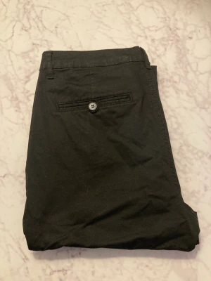 Svarta Chinos - Chinos med bra kvalitet, använda några fåtal gånger. Straight leg passform. Är personligen storlek 32 och dom passar bra för mig, så storleken är mindre än den verkar.