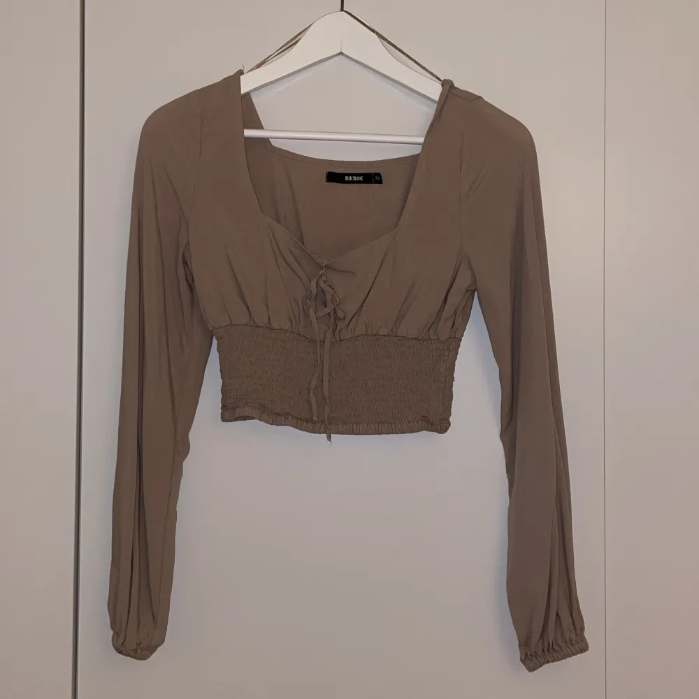 En beige/brun topp med en knytning fram från bikbok😍☺️. Toppar.