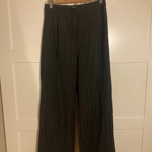 Randiga kostymbyxor  - Svarta raka kostymbyxor med vita/gråa ränder från Bershka i storlek 38, nypris 399kr. Har inga fickor. Är i bra skick. Frakt tillkommer!!!