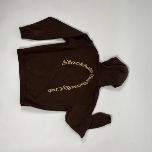 Stockholm Surfboard Club - Asnice hoodie från Stockholm Surfboard Club! Brun med gult tryck