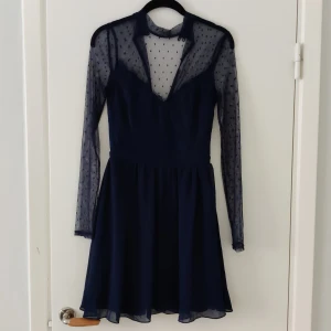 NELLY festklänning  - En mörkblå festklänning som man knäpper i nacken där bak, den är relativt kort och see-through överdel. 