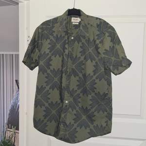 Mörkgrön kortarmad skjorta (herr) med mörkblå detaljer. Lätt använd Storlek: Regular fit (M)