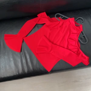 Röd festlig topp med volanger - Röd festlig top med bara axlar, ser väldigt fin ut när man tar på sig den. Helt oanvänd m. etikett. Säljer pga fel storlek