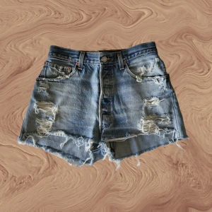 Vintage Levi's jeansshorts - Trendiga och "slitna" vintage Levi's-shorts omgjorda från jeans. Köpta i affär. Eftertraktad hourglass-modell som ger en superfin form och sitter riktigt snyggt! Lite för små för mig dock. Storlek: W26/W27. Nyskick. Mått skickas på begäran.