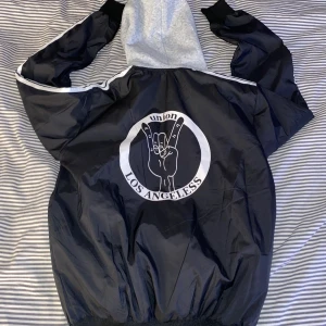 Jacka med tryxk - Snygg tunn jacka med grå huva. Aldrig använd mer än provad. Vet ej storlek då det ej står något men skulle säga xs/s