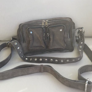 Núnoo väska - Väska i toppskick från Núnoo. Materialet är grå mocka och köpt från Nelly.com.  Köpt för 1600 SEK.