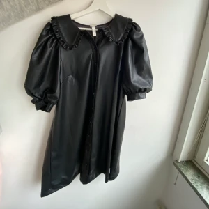 HELT NY klänning i läder imitation - Svart klänning från HM. Helt oanvänd. Superfin krage och ärmar. Passar M men den är lite stor i storleken. Perfekt för wednesday addams outfiten!!
