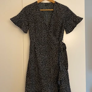 Prickig omlottklänning S - Svart omlottklänning med vita prickar. Kort ärm och volanger. Använd ett fåtal ggr och i mycket bra skick! Storlek S.