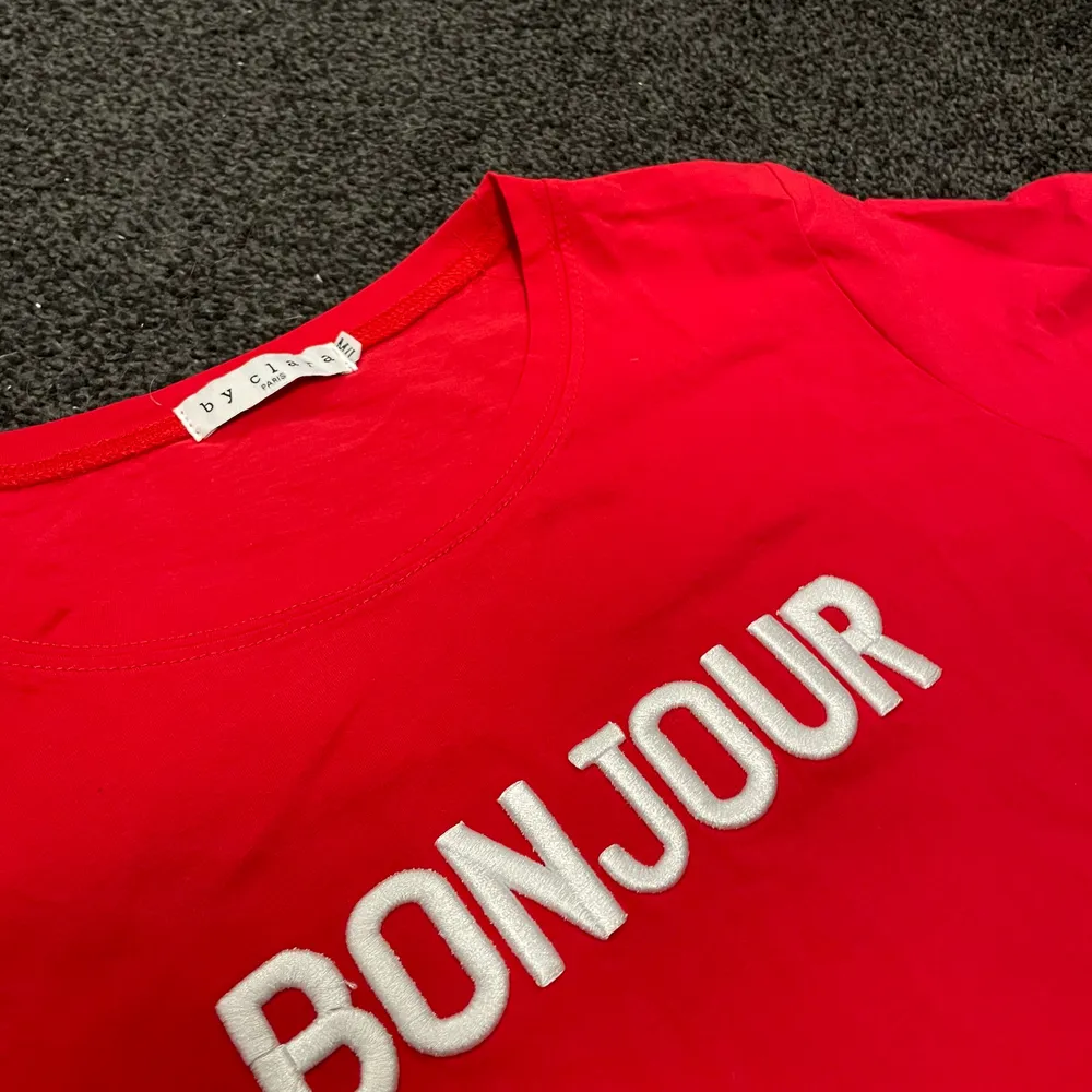 Röd t-shirt med texten ”Bonjour”. Knappt använd och i storlek S. Perfekt till vita jeans och någon härlig röd detalj. Även fint till blå eller svarta jeans. Färg är ju bara för underbart!!. T-shirts.