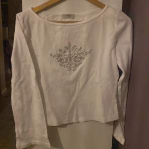 Långärmad vit tröja med vida ärmar och lite kroppad. Med vit silver detalj. Frakt ingår inte!💞